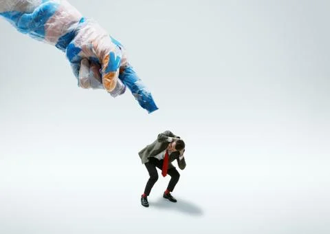Young caucasian man avoiding big plastic hand on white studio background Stock Photos