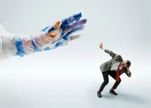 Young caucasian man avoiding big plastic hand on white studio background Stock Photos