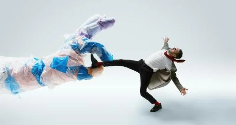 Young caucasian man avoiding big plastic hand on white studio background Stock Photos