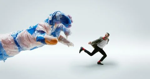 Young caucasian man avoiding big plastic hand on white studio background Stock Photos