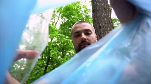 A young Caucasian man with a beard puts a plastic bottle in a trash bag. Stock Footage 132137093