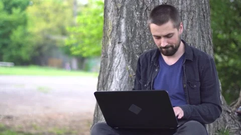 A young caucasian man with a beard is sitting under a tree Stock Footage 130353602