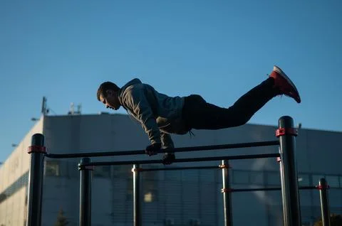 Young caucasian man doing parallel bars exercise outdoors. Stock Photos