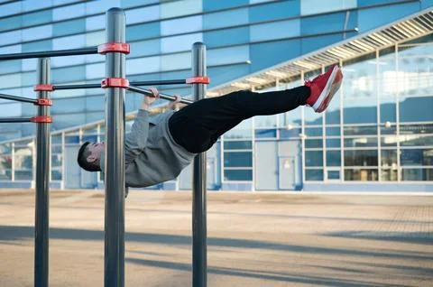 Young caucasian man doing parallel bars exercise outdoors. Stock Photos