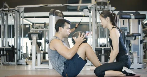 Young caucasian man doing sit-ups with a ball next to his personal trainer in fi Video stock 102976774
