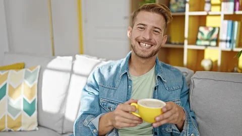 Young caucasian man drinking coffee sitting on sofa at home Video stock 247380526