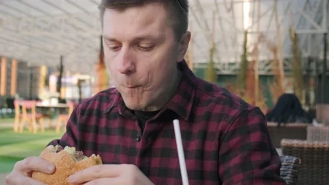 Young Caucasian man eats meat burger and drinking cola in fast food restaurant Stock Footage 236632739