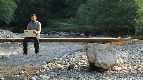 Young caucasian man freelancer working remote on laptop computer near wild river 스톡 동영상 137537017