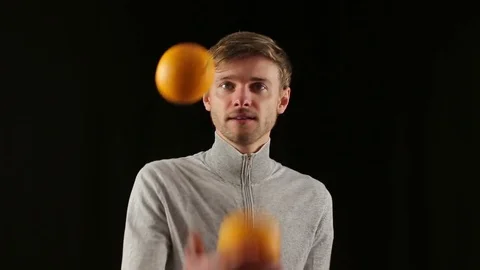 Young caucasian man juggling oranges close up portrait isolated in black Stock Footage 82919421