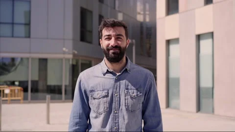 Young caucasian man looking at camera with cheerful smile near big office bui Stock Footage 153251218