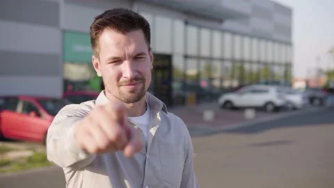 A young Caucasian man points at the camera and nods in an urban area - a 스톡 동영상 147946530