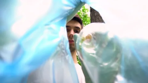 A young Caucasian man puts a plastic bottle in a trash bag. Stock Footage 132137221
