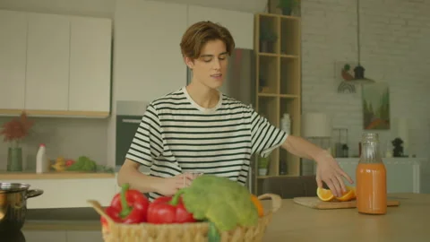 Young Caucasian man putting slice of orange on plate in kitchen. Guy drinking Stock Footage 314557614