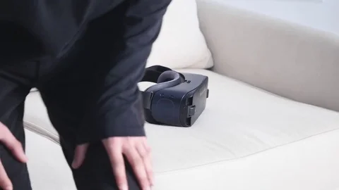 Young Caucasian man sits on sofa and having fun using white VR headset glasses Video stock 73036016