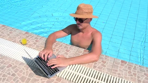 Young Caucasian man in straw hat in pool is working on laptop, typing message Stock Footage 147945367