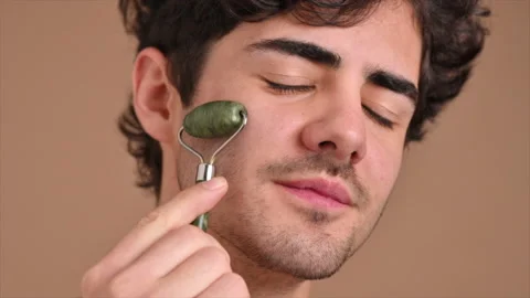 A young caucasian man with stubble beard is doing a facial massage using a Stock Footage 221127983