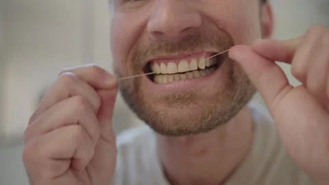 Young caucasian man using dental floss to clean his teeth while looking in the 스톡 동영상 335151782