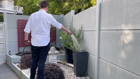 Young caucasian man using a hose to water herbs in planters in a small, oriental Stock Footage 171907761