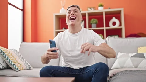 Young caucasian man using smartphone sitting on sofa with winner gesture at.. Video stock 246145293