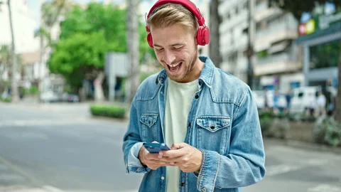 Young caucasian man using smartphone wearing headphones at street Stock Footage 247380494