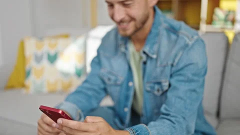 Young caucasian man using smartphone sitting on sofa at home Stock Footage 247380525