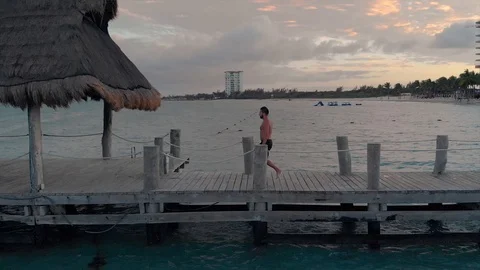 A young caucasian man walking diving off of a dock into the ocean near a Stock Footage 104130189