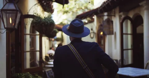 Young caucasian man walking through alley in shadow and playing guitar Video stock 146931959