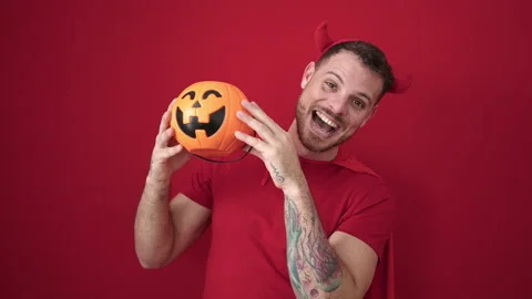 Young caucasian man wearing devil costume covering face with pumpkin over i.. Stock Footage 232871895