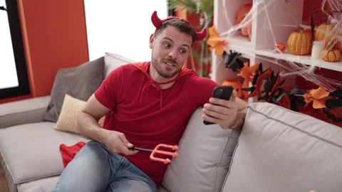 Young caucasian man wearing devil costume sitting on the sofa doing video c.. Stock Footage 236551670