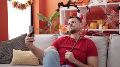 Young caucasian man wearing devil costume sitting on the sofa using smartph.. Stock Footage 237836896