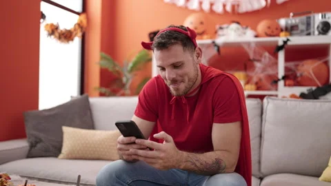 Young caucasian man wearing devil costume sitting on the sofa using smartph.. Stock Footage 238608206