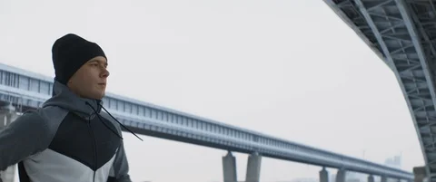 Young caucasian strong runner jogs along embankment of big city in cold winter Stock Footage 120299139