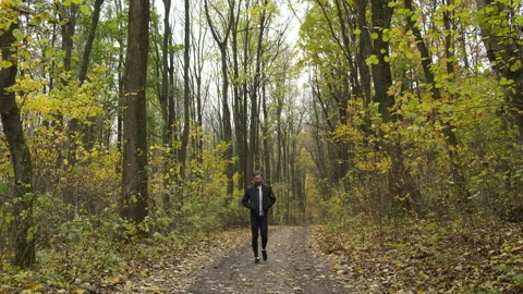 A young Caucasian walks in an autumn park and listens to music on headphones Stock Footage 143594553