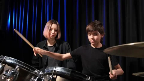 Young caucasian woman teaches a boy to play the drums in the studio on a black Stock Footage