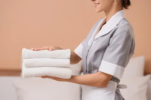 Young chambermaid with stack of clean towels in hotel room Stock Photos