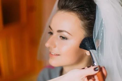 Young charming bride applying wedding make-up by professional artist Фото