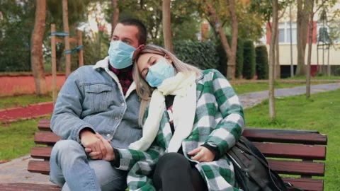 Young charming couple sitting on a bench in park, wearing protective masks Stock Footage 143705107