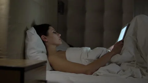 Young charming girl are using digital tablet on the bed before she sleeping at Stock Footage 88850604