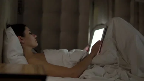 Young charming girl are using digital tablet on the bed before she sleeping at Stock Footage 88851283