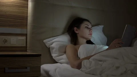Young charming girl are using digital tablet on the bed before she sleeping at Stock Footage 88889481