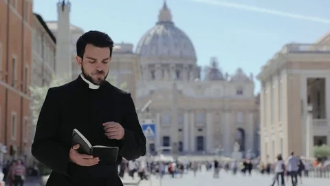 Young charming priest scrolls the gospels and smiles at the camera- Saint Peters Stock Footage 76438661
