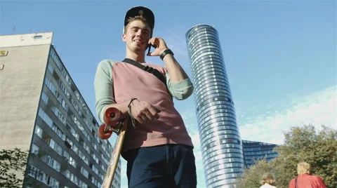 Young cheerful boy with longboard talking by phone in the city street. Stock Footage 43221983