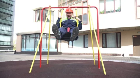 A young cheerful builder swings on a swing in a residential yard. Stock Footage 130140578