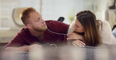 Young cheerful couple lying on sofa listening music on smartphone Stock Footage 77410905