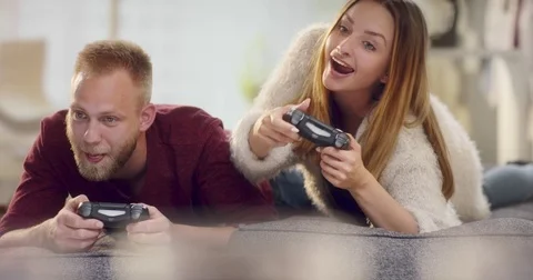 Young cheerful couple lying on sofa teasing each other while playing video ga Stock Footage 77411261