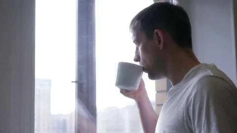 A young cheerful man drinks from a white cup, tea or coffee. 4k, 3840x2160. HD Stock Footage 75036281