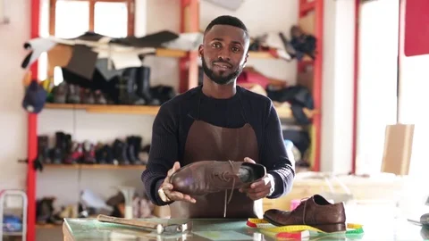 Young  cheerful shoemaker in workshop holding shoes. Stock Footage 104983236