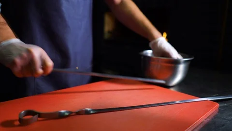 Young chef in apron and gloves puts pieces of marinated meat on skewer Stock Footage 99788116