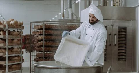 Young chef baker with a beard preparing the dough add some more flour in a big Stock Photos