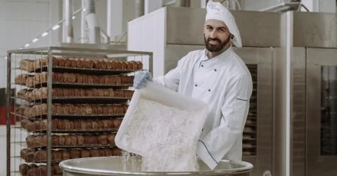 Young chef baker with a beard preparing the dough add some more flour in a big Stock Photos